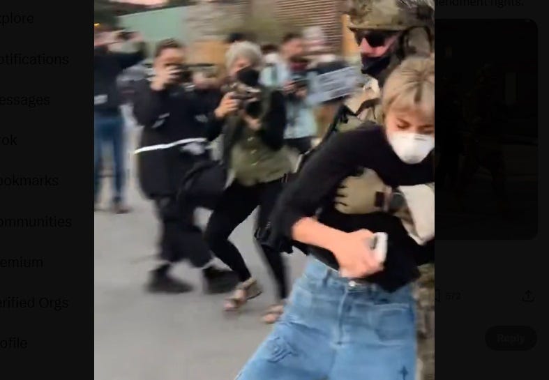 video screenshot showing a masked ICE cop in full battle gear grabbing congressional candidate Kat Abughazaleh, a young woman in jeans and black sweatshirt, dragging her away from the entrance to a detention center. behind them, journalists are photographing and recording the scene. Seconds afterward, he threw her down on the pavement. video screenshot showing a masked ICE cop in full battle gear grabbing congressional candidate Kat Abughazaleh, a young woman in jeans and black sweatshirt, dragging her away from the entrance to a detention center. behind them, journalists are photographing and recording the scene. Seconds afterward, he threw her down on the pavement.