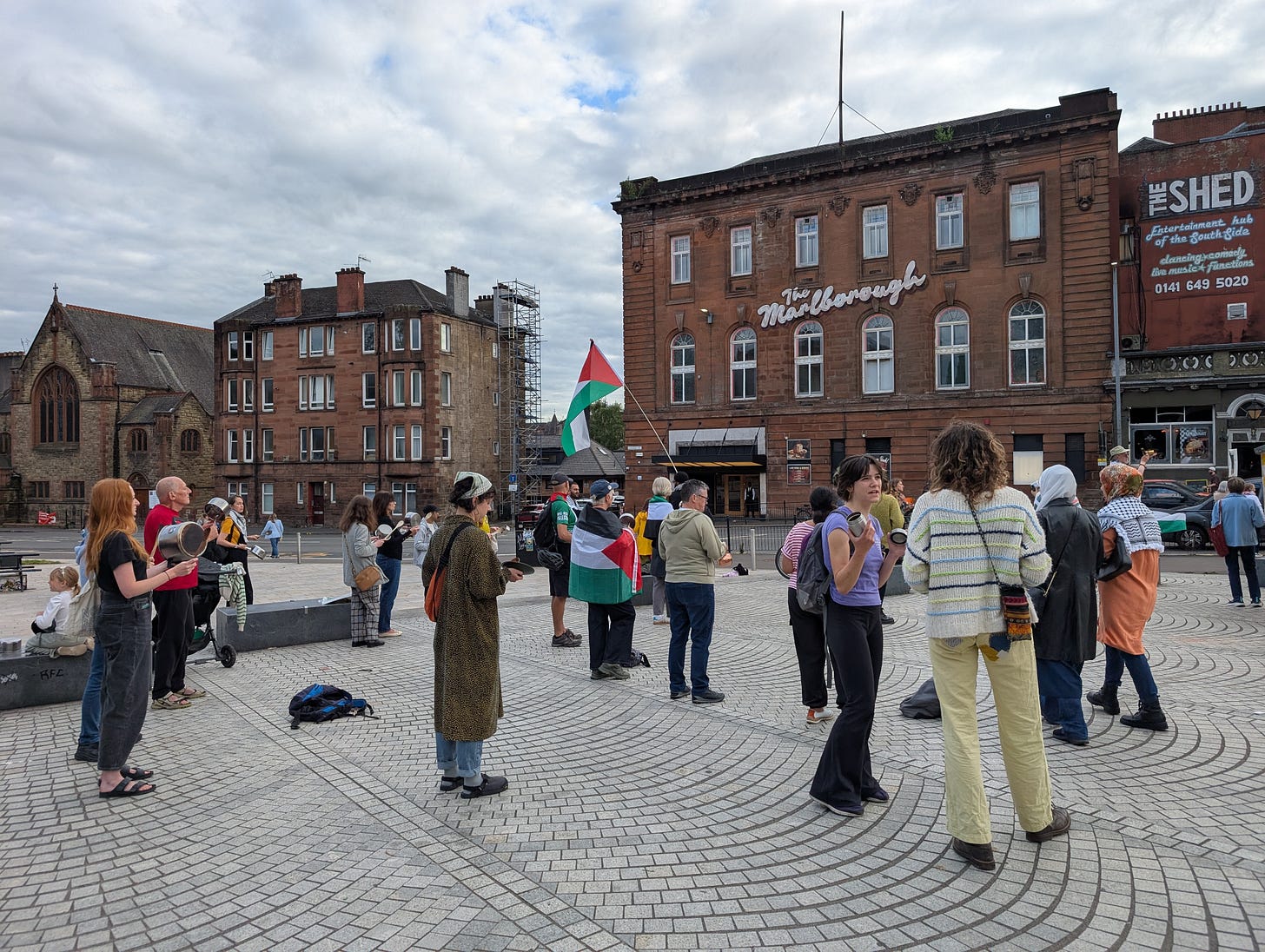A couple dozen people gathered outside Langside Hall, banging pots. There are some Palestine flags.