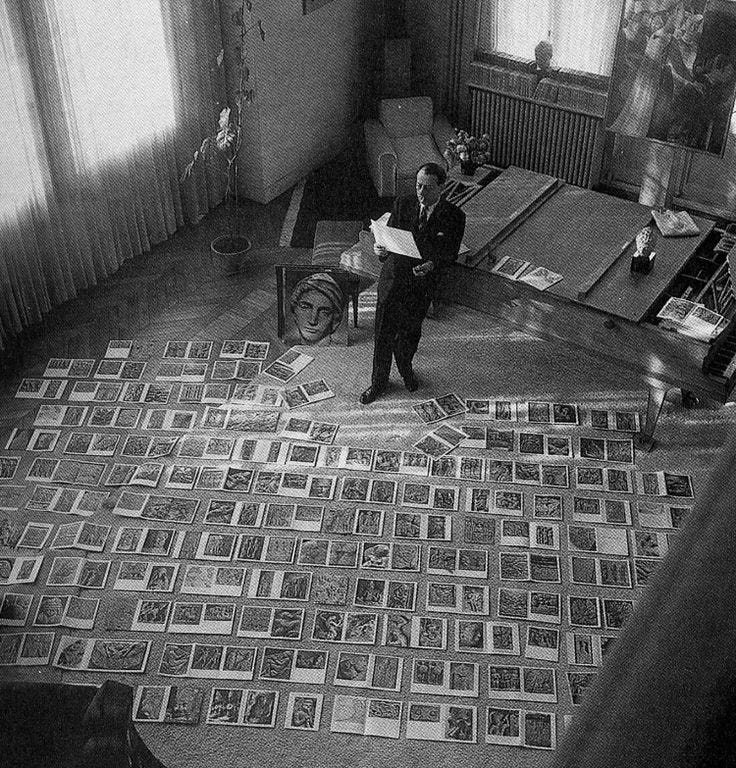 This may contain: black and white photograph of man standing in room with many framed photographs on the floor