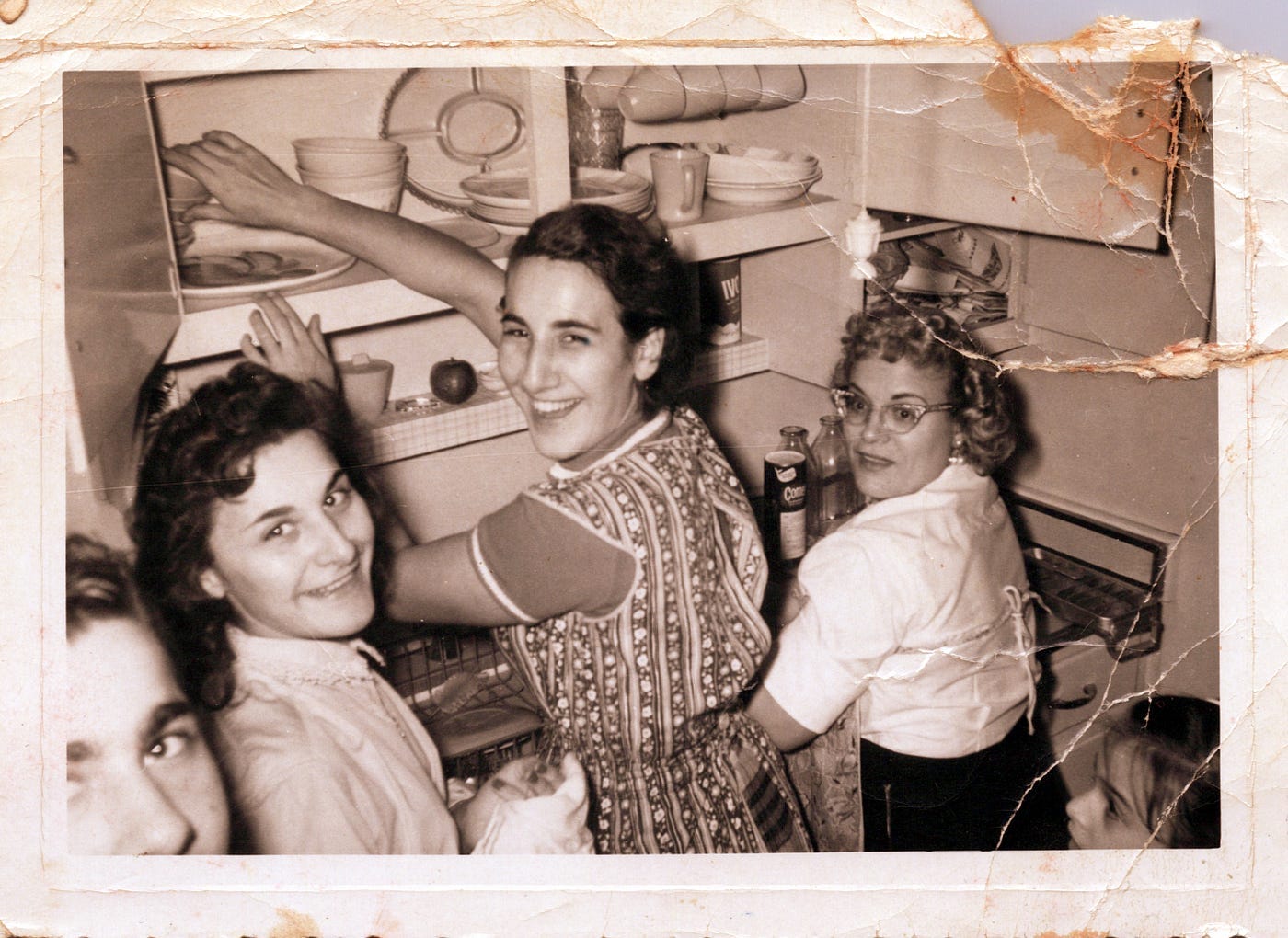 Photo of three women laughing while putting away dishes in a kitchen cabinet