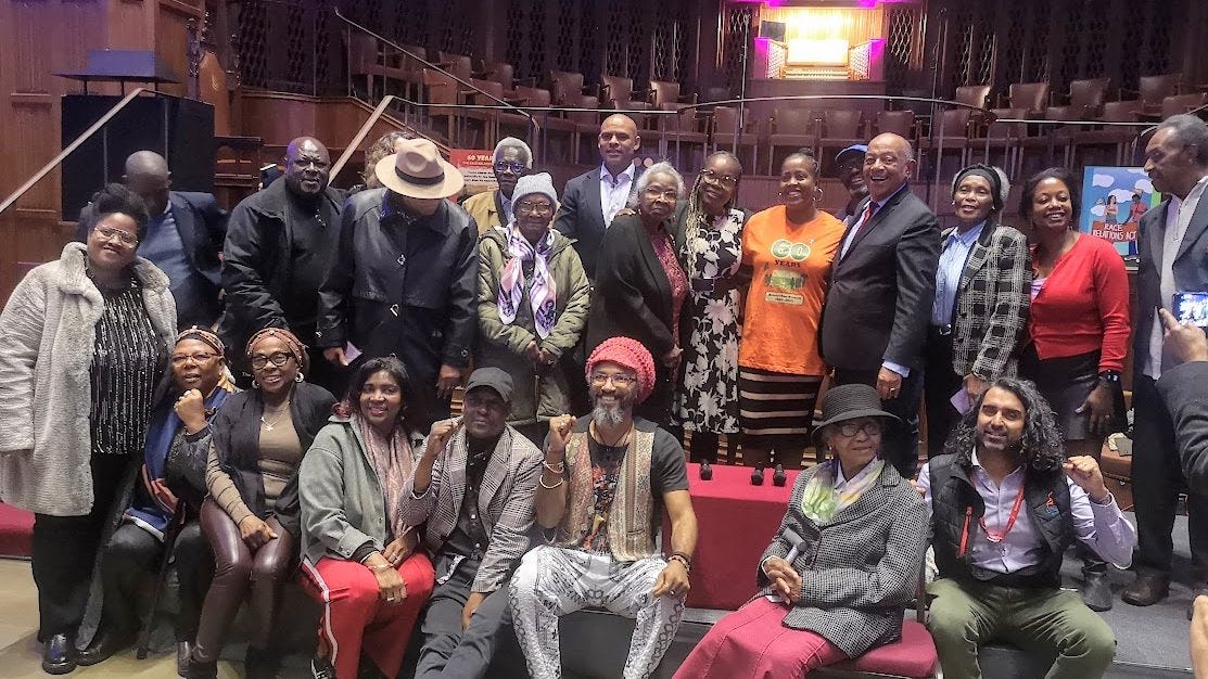 A large group of community members, activists and civic leaders gathered at the Wills Memorial Building in Bristol for the Talks4Change: Pioneers of Progress event in November 2025, marking 60 years since the Race Relations Act. Several attendees wear orange t-shirts reading "60 Years." A Race Relations Act banner is visible in the background. Photo credit: Milan Perera.