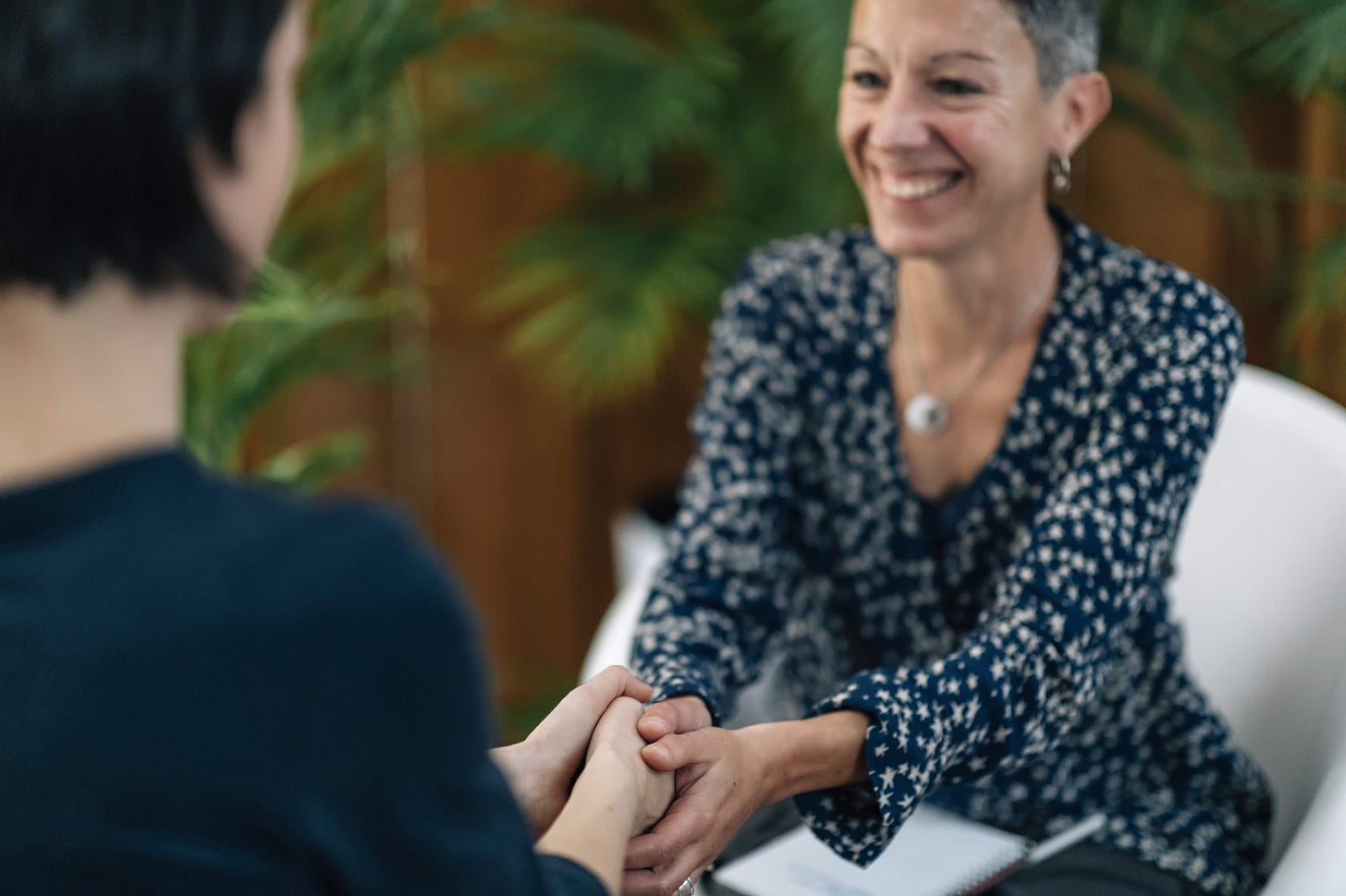 A life coach smiles and shakes the hand of her new client, whose back is to the camera. A life coach smiles and shakes the hand of her new client, whose back is to the camera.