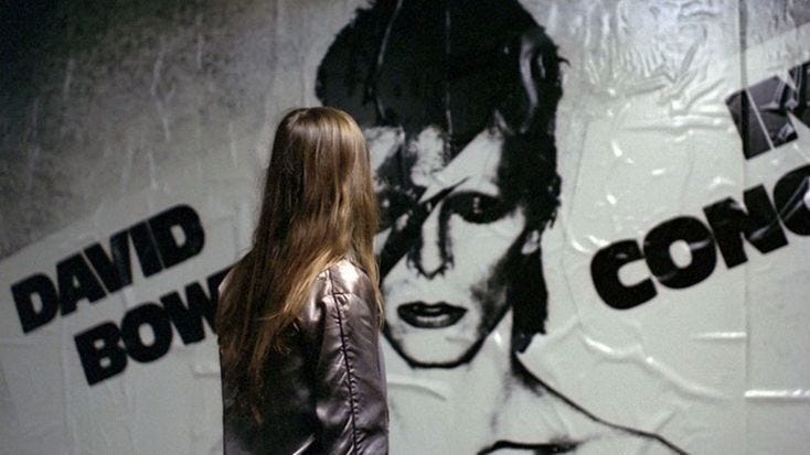 This may contain: a woman standing in front of a wall with a poster on it's side