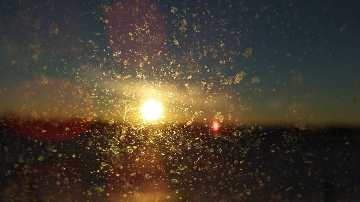 A sunset seen through dirty glass, but the image is focused on the blemishes of the glass rather than the pretty sunset out of focus in the distance. 