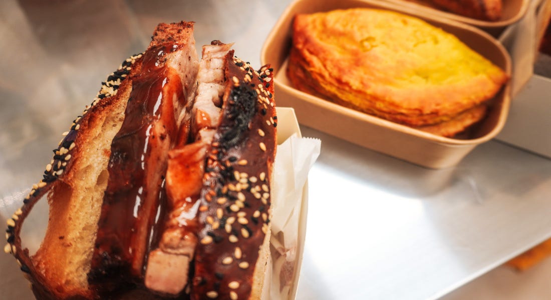 A pork sandwich in coco bread next to a yellow Jamaican patty