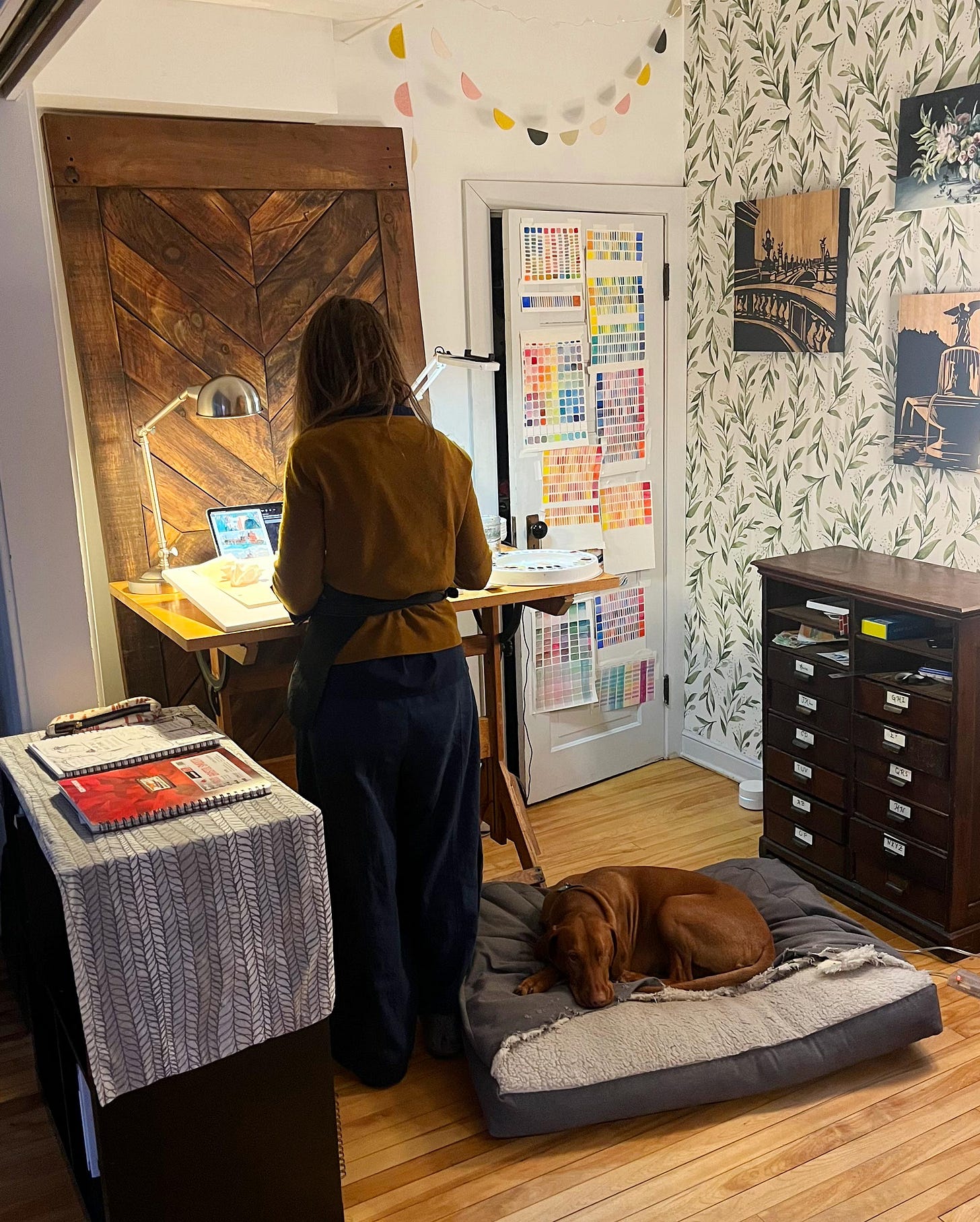 Graphic novelist K. Woodman-Maynard creates in her studio as Lief the one-eyed Visla takes a nap on his doggy bed. 