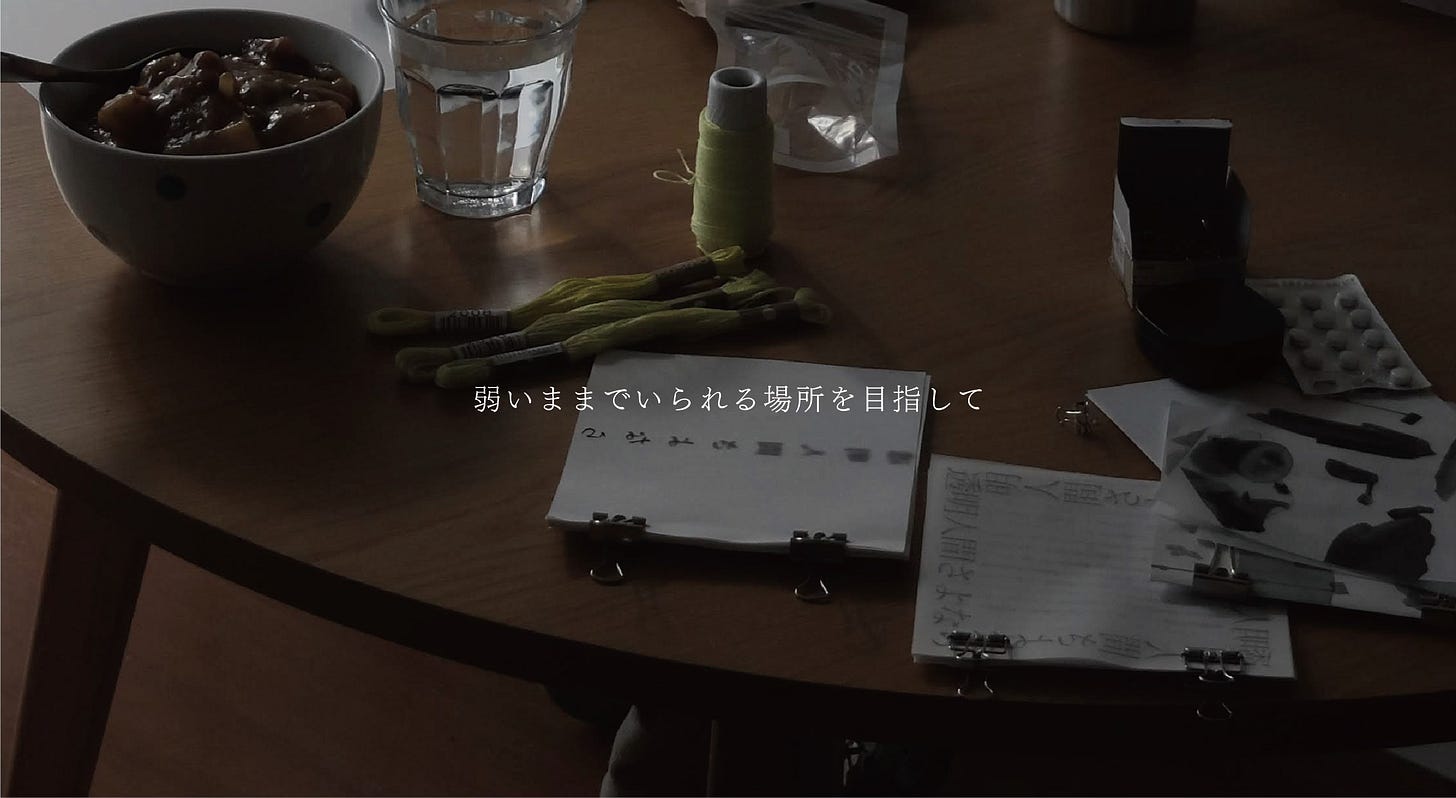 連載ヘッダー画像。暗い室内にある丸型のテーブルがアップで写っており、机上には食事と薬、作りかけと思しきZINEなどが置いてある。