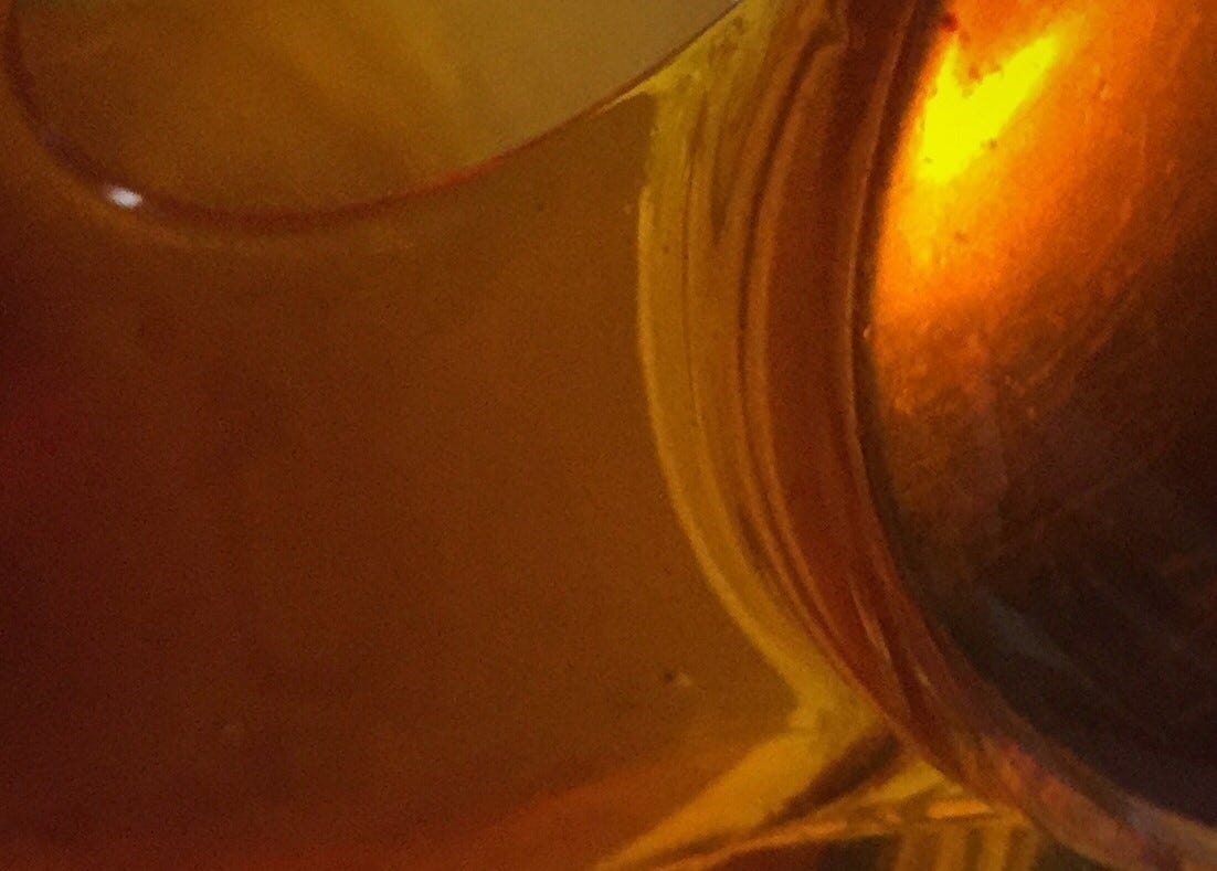 close up of honey dripping from a spoon, taken so close up that the context (the spoon) is not visible, just colours and textures and little glints of light