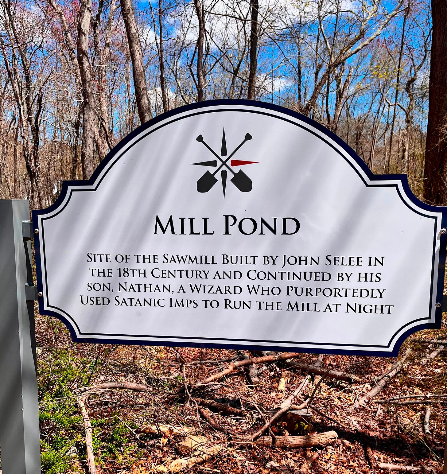 A historic sign in the woods. Text reads: "Site of the sawmill built by John Selee in the 18th century and continued by his son, Nathan, a wiaard who purportedly used satanic imps to run the mill at night." Easton, Massachusetts. 