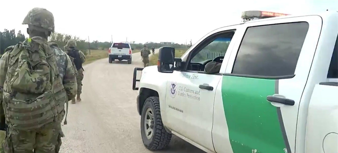 Texas National Guard Soldiers assigned to "Operation Lone Star" patrol a border road on foot as US Border Patrol vehicles pass by.