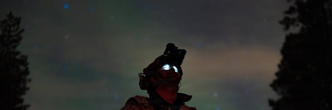 Soldier wearing night vision goggles under the aurora borealis.