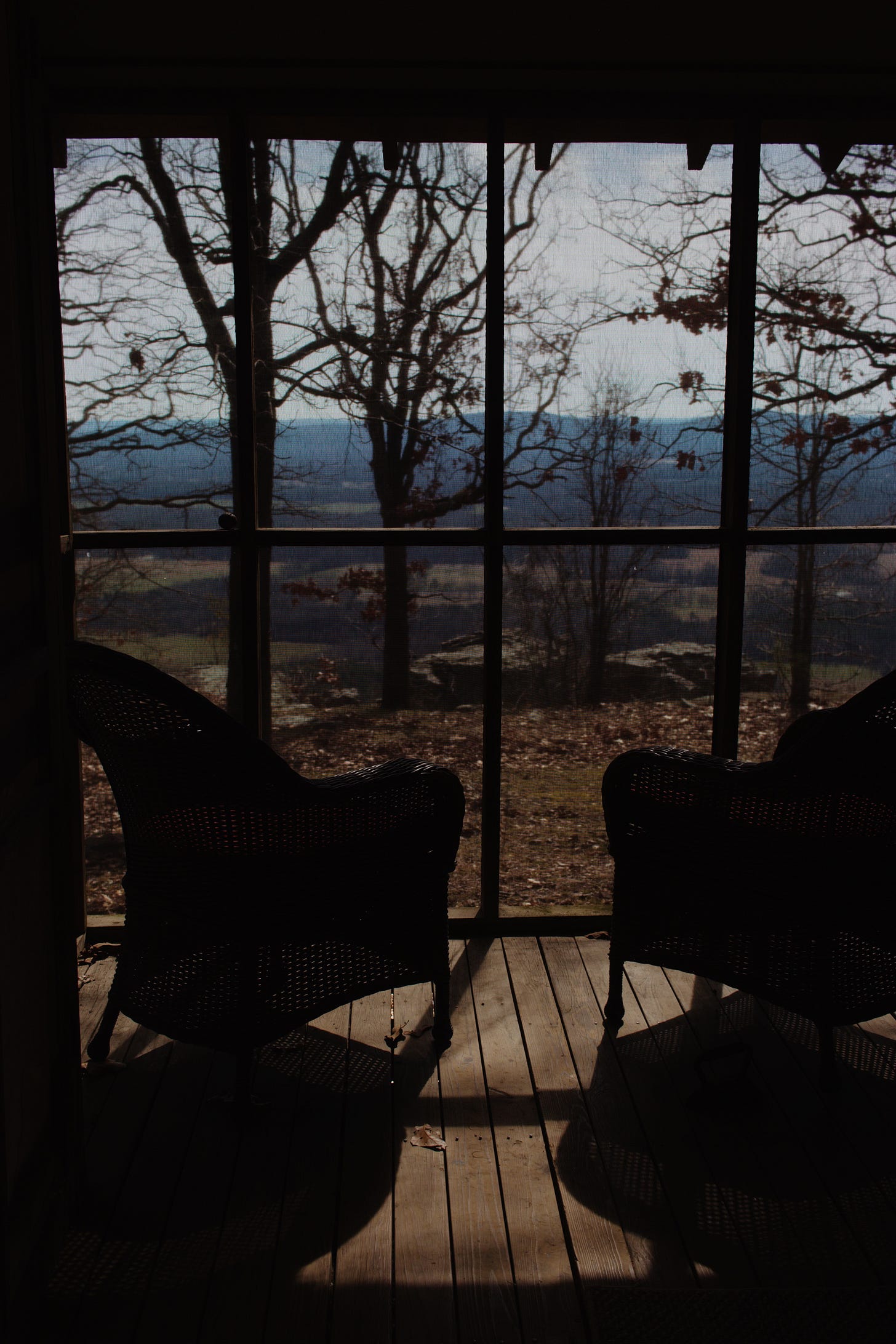 Screened in cabin porch with two wicker chairs looking out on the Petit Jean Mountains