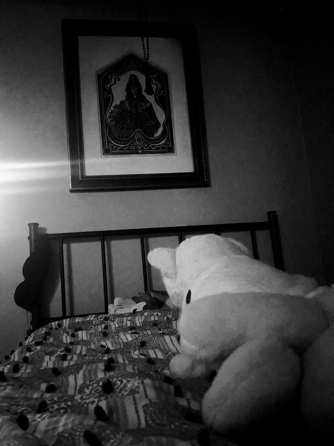 a nine-tailed fox stuffy sits on a bed before a woodblock print that doubles as a protective talisman which hangs on the wall above the headboard