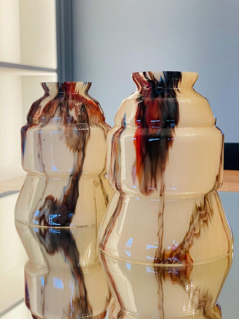 May include: Two glass vases with a cream colored base and brown, red, and black marbled designs.