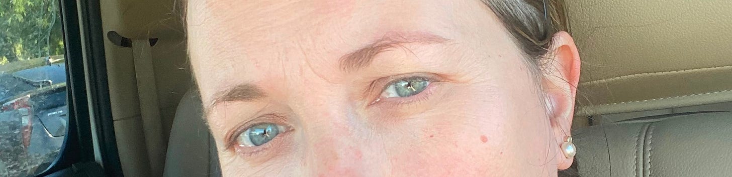 Cropped out photo of the author's eyes the day. Her eyes are blue green. She is white with brown hair. She has two piercings in her left ear. She appears to be sitting in her car.