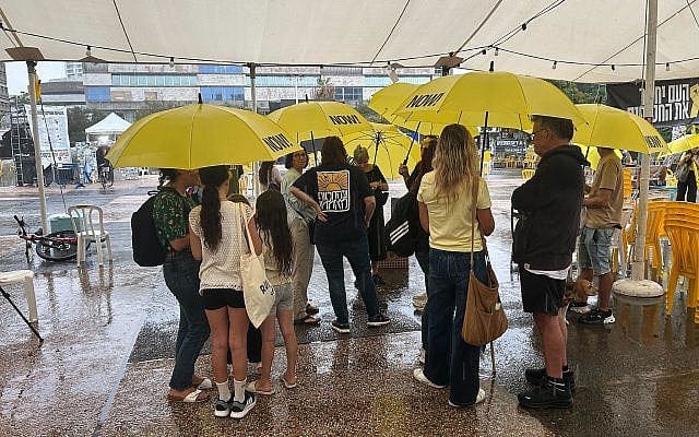 People shelter from the rain in Tel Aviv's Hostages Square on October 9, 2025. (Ben Sales/Times of Israel)