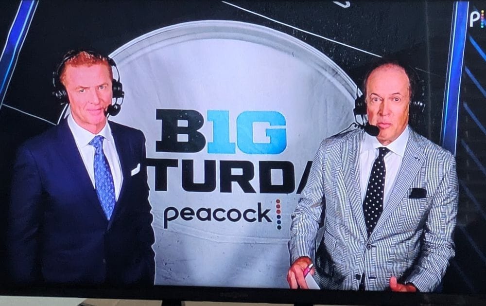 Sportscasters in front of a sign that reads BIG TURD, cutting off the word SATURDAY