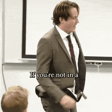 a man in a suit and tie stands in front of a white board with the words if you 're not in a written on it