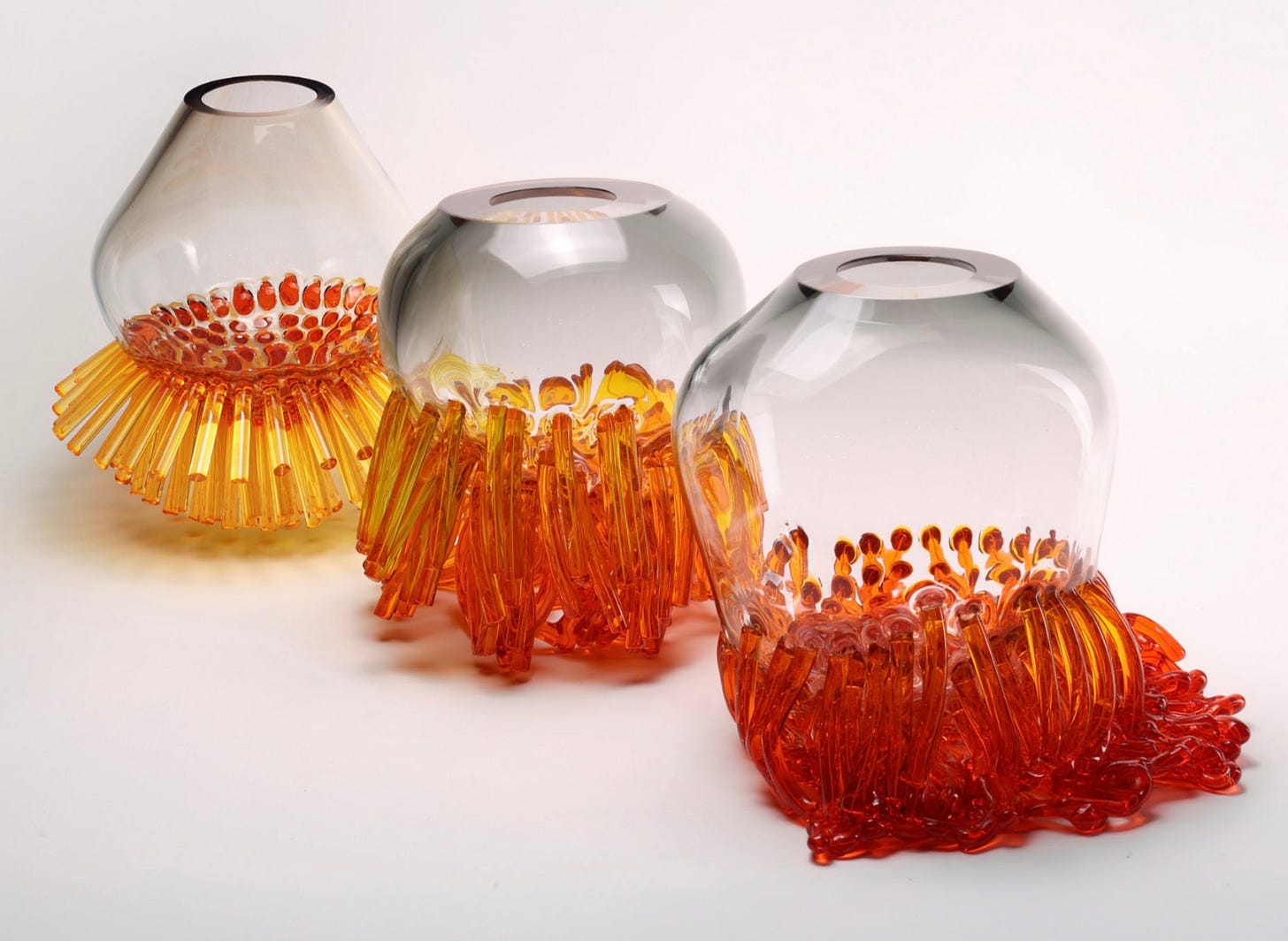 Pieces from the Echinozoa collection: three clear glass vessels with fringes of amber and red glass canes at the base Pieces from the Echinozoa collection: three clear glass vessels with fringes of amber and red glass canes at the base