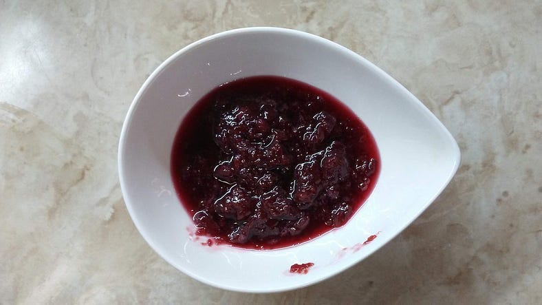 A white bowl on a counter, containing purple-red cherry bits and jam.