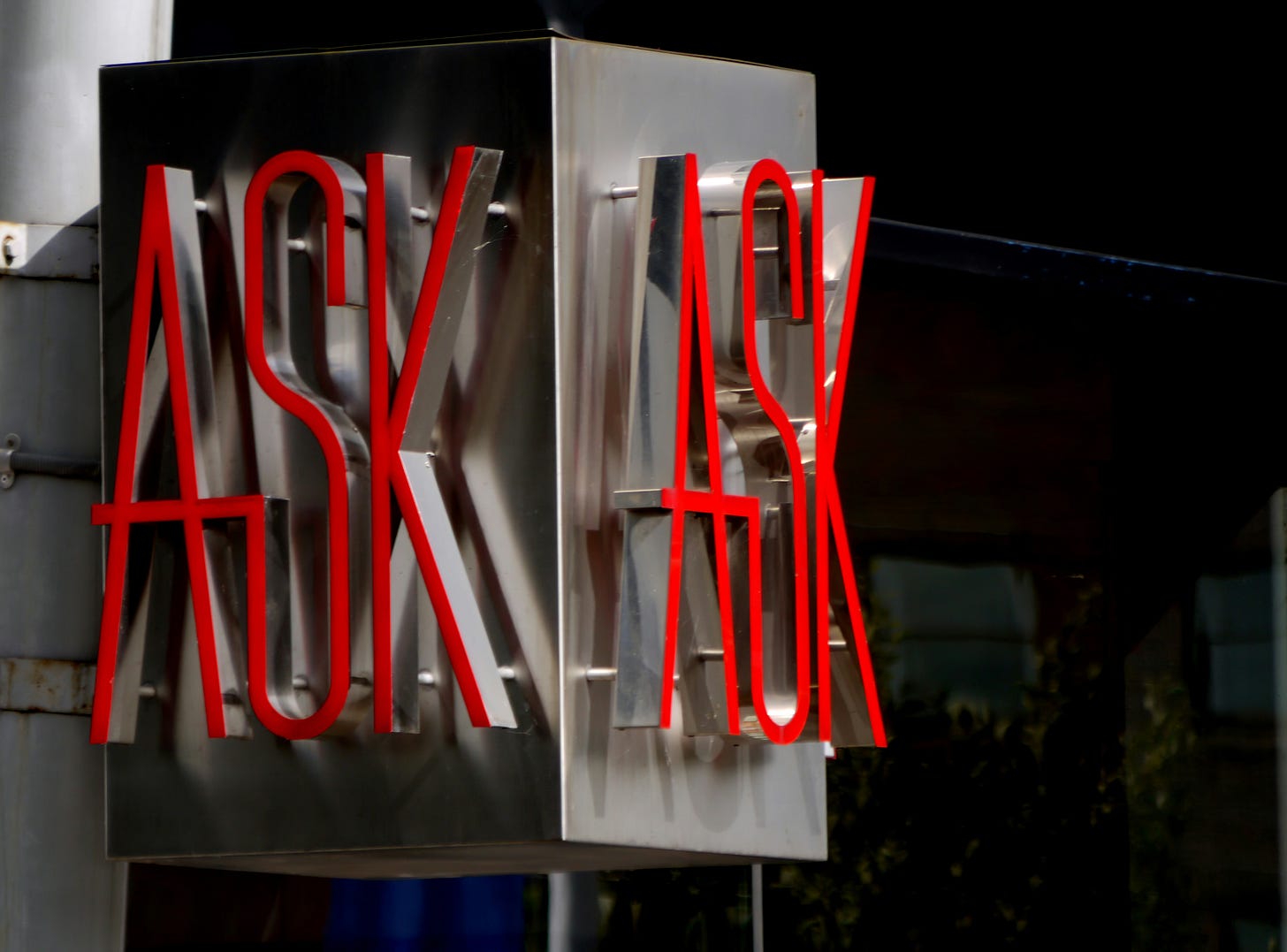 A two sided neon sign with red letters that read ASK. 