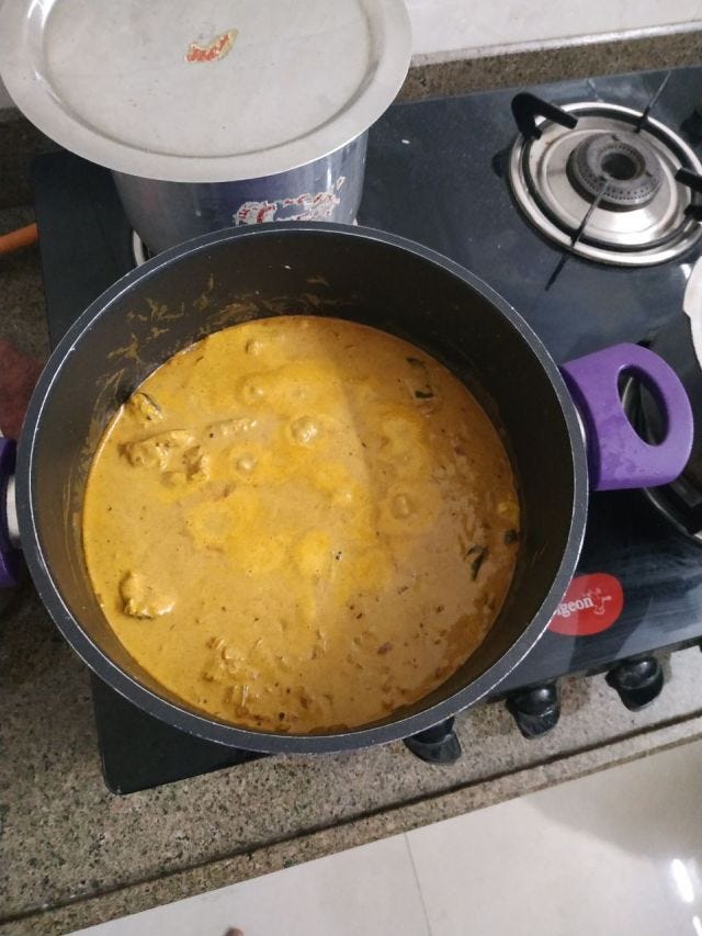 A black and purple vessel that contains a mustard colour fish curry.