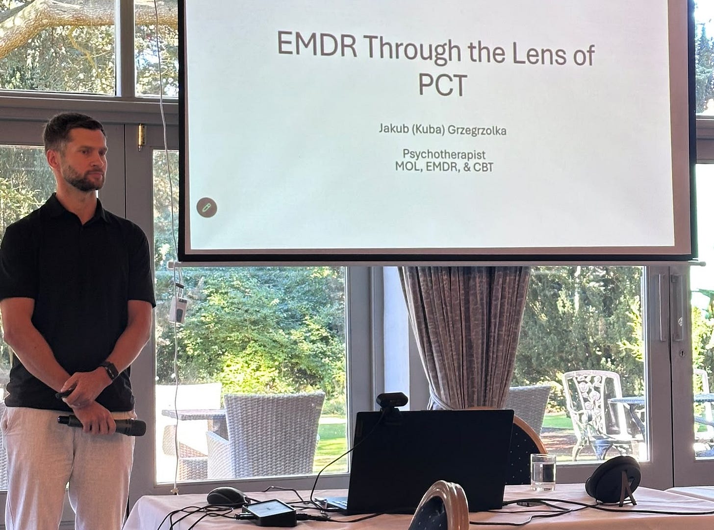 Kuba holding a microphone beside a presentation slide titled “EMDR Through the Lens of PCT” at the IAPCT 2026 conference in York..