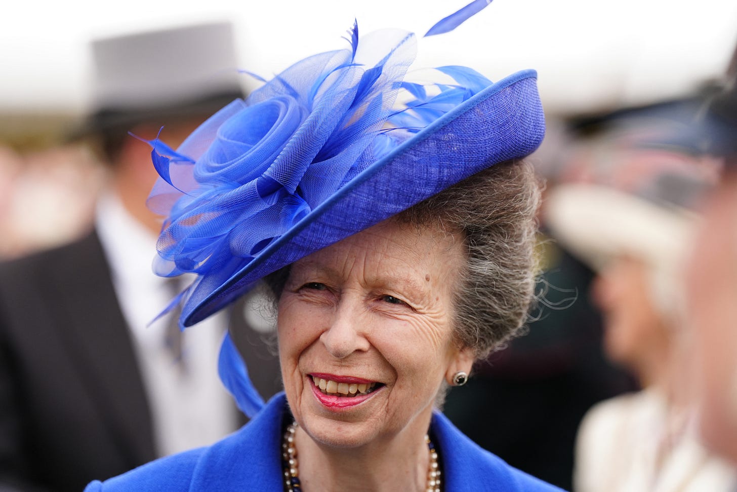 Princess Anne smiling in blue coat and feathered hat
