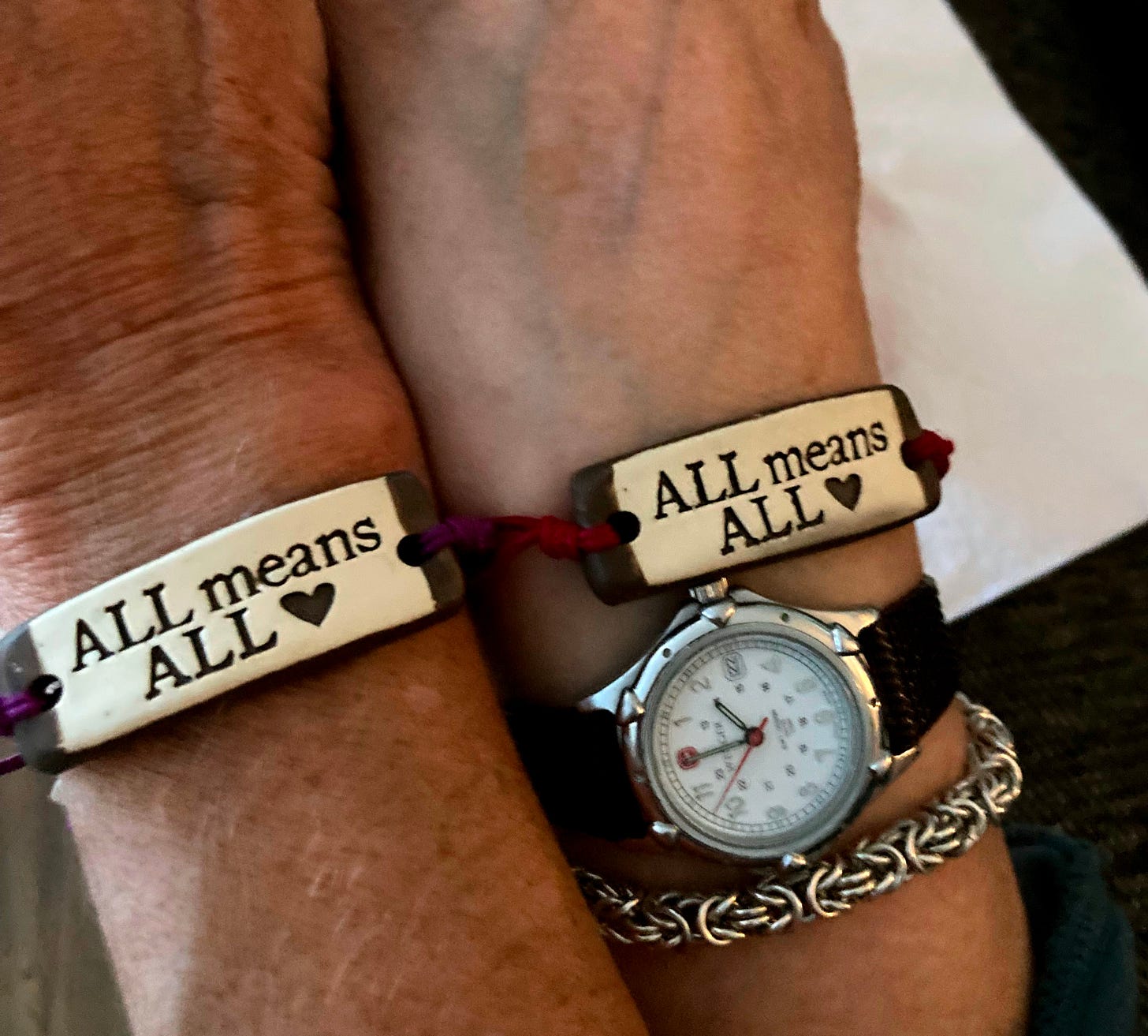 All Means All: picture of two wrists displaying a bracelet that reads "All Means All"