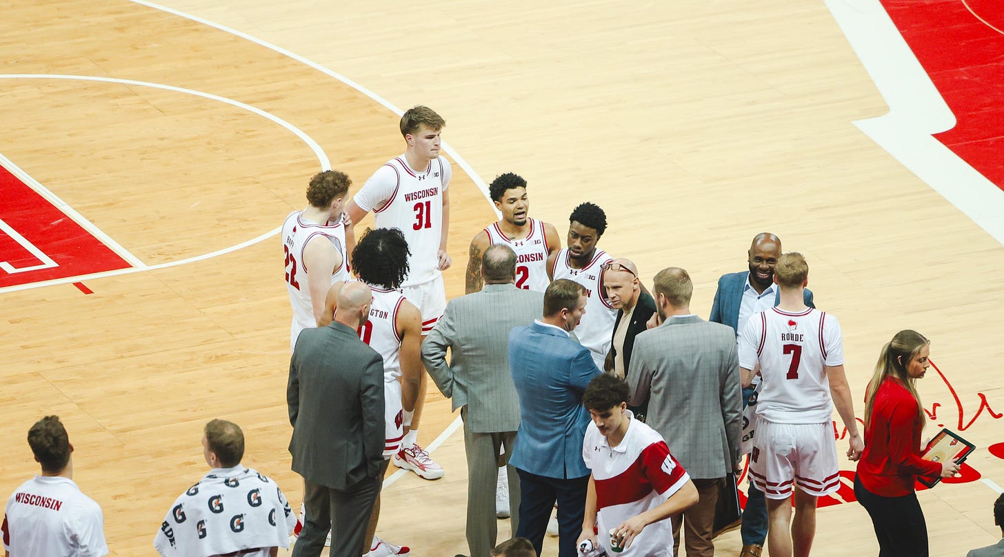 Wisconsin Badgers basketball players talking with coaches on the sideline during a game at the Kohl Center.