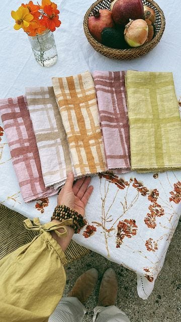 This may contain: a person sitting at a table with some cloths on it and fruit in a basket