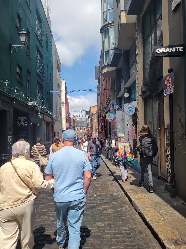 Five photos from the Irish Rock and Roll Museum and Temple Bar district. First, my daughter next to a photo of the band, U2. A display of three vintage guitars. The museum's Wall of Fame exterior and a streetscape in Temple Bar.