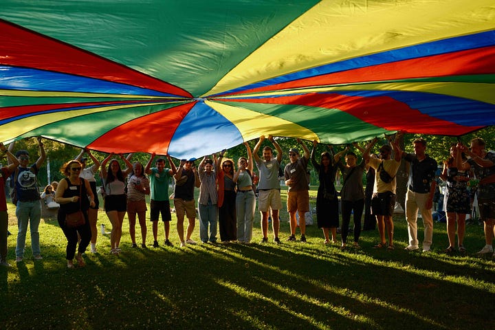 Two pictures taken at Hidden Rivers' kick-off celebration in Christie Pitts park. One is the words "You Gotta Explore Your City: HIdden Rivers Kick-Off Celebration 2025", written in letters that have been un-scrambled from a scavenger hunt. The other shows a group of people about to go under a rainbow parachute.