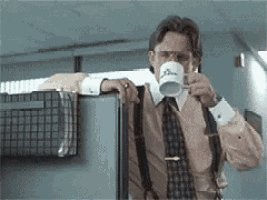 a man in a suit and tie is drinking a cup of coffee while leaning on a cubicle . a man in a suit and tie is drinking a cup of coffee while leaning on a cubicle .