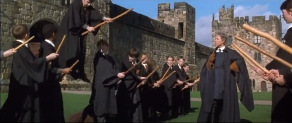 A group of robed students stand on broomsticks A group of robed students stand on broomsticks