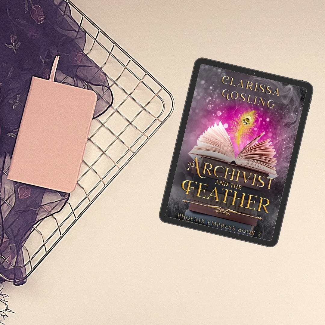 A tablet showing the cover of The Archivist and the Feather by Clarissa Gosling alongside a pink notebook, a purple fabric and a wire tray