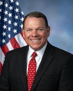 portrait of Rep. Sam Graves in a dark suit and red tie before a U.S. flag. 