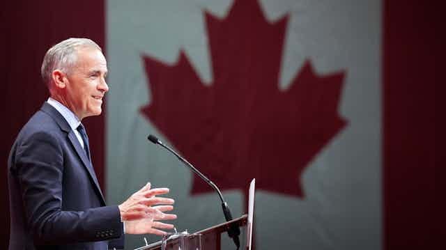 A man stands in front of a podium with a large Canadian flag beside him.