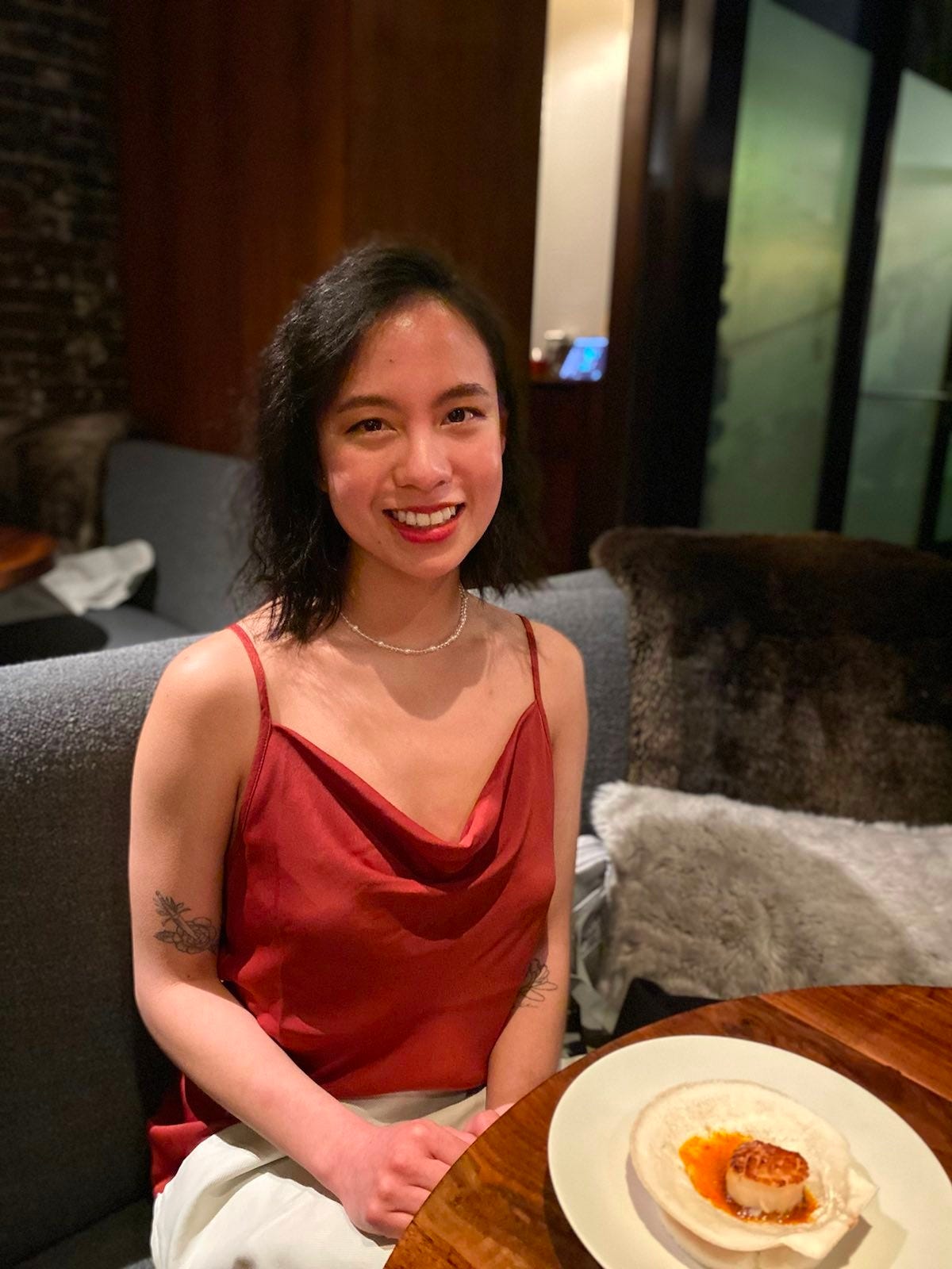 The author, Mary, wearing a red dress and smiling at the camera. She's sitting at restaurant table with a scallop dish in front of her.