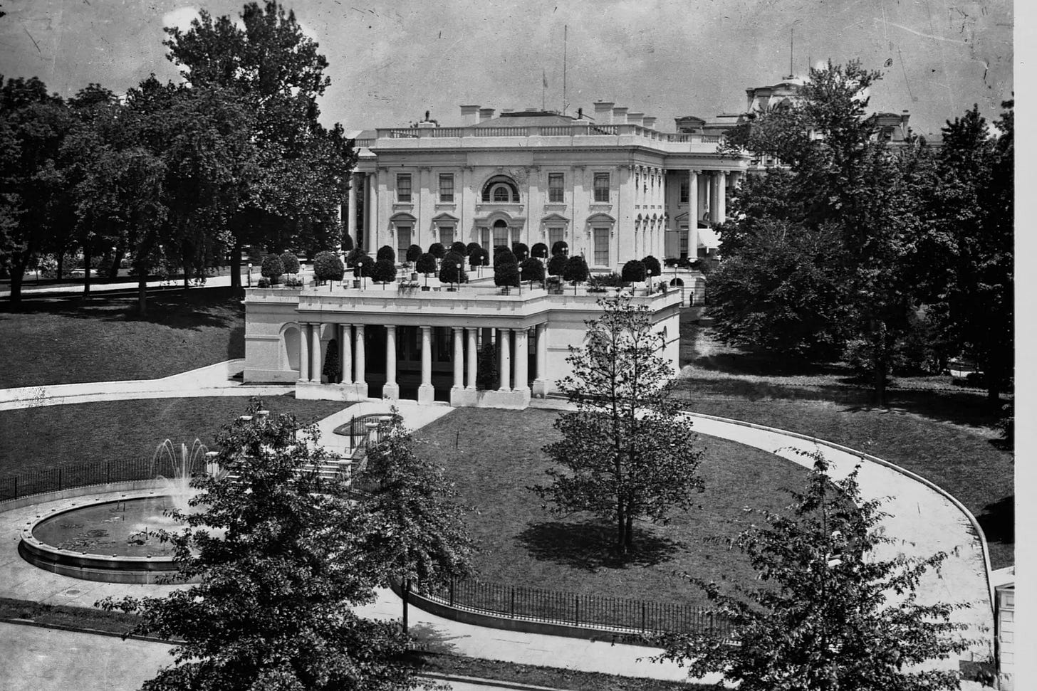 photo of the single-story East Terrace building in 1902, with a row of columns and potted trees on the roof