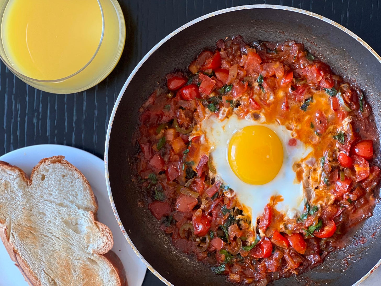 A hearty serving of shakshuka, with eggs nestled in a rich tomato and vegetable sauce, plated alongside two slices of Challa bread and a glass of freshly squeezed orange juice. The dish captures the essence of a homemade breakfast made by Liat Portal, showcasing the comfort and vibrance of Israeli flavors. Foodie Disorder featured this as an iconic breakfast delight.