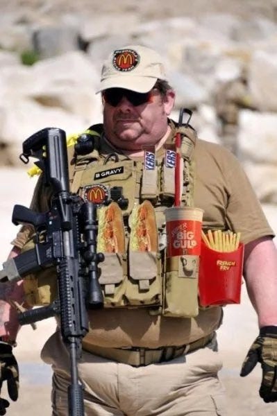 A person wearing a tactical vest with McDonald\'s logos, holding a rifle and fast food items including fries and a drink. The vest has a name patch reading "B. Gray" and various pouches. The person wears a beige cap with a McDonald\'s logo, sunglasses, and gloves, standing in a rocky outdoor setting. A person wearing a tactical vest with McDonald\'s logos, holding a rifle and fast food items including fries and a drink. The vest has a name patch reading "B. Gray" and various pouches. The person wears a beige cap with a McDonald\'s logo, sunglasses, and gloves, standing in a rocky outdoor setting.