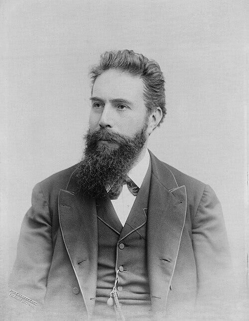 Black-and-white studio portrait of Wilhelm Röntgen, seated in a three-piece suit with a full beard, looking slightly to his right. Black-and-white studio portrait of Wilhelm Röntgen, seated in a three-piece suit with a full beard, looking slightly to his right.