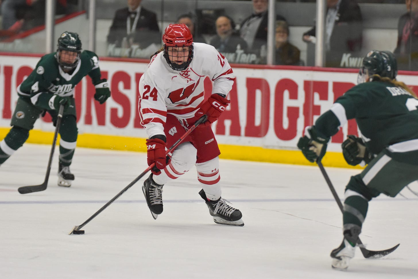 Wisconsin Badgers winger Charlotte Pieckenhagen facing toward the camera with the puck on her stick. Two Bemidji State Beavers defenders are in the frame