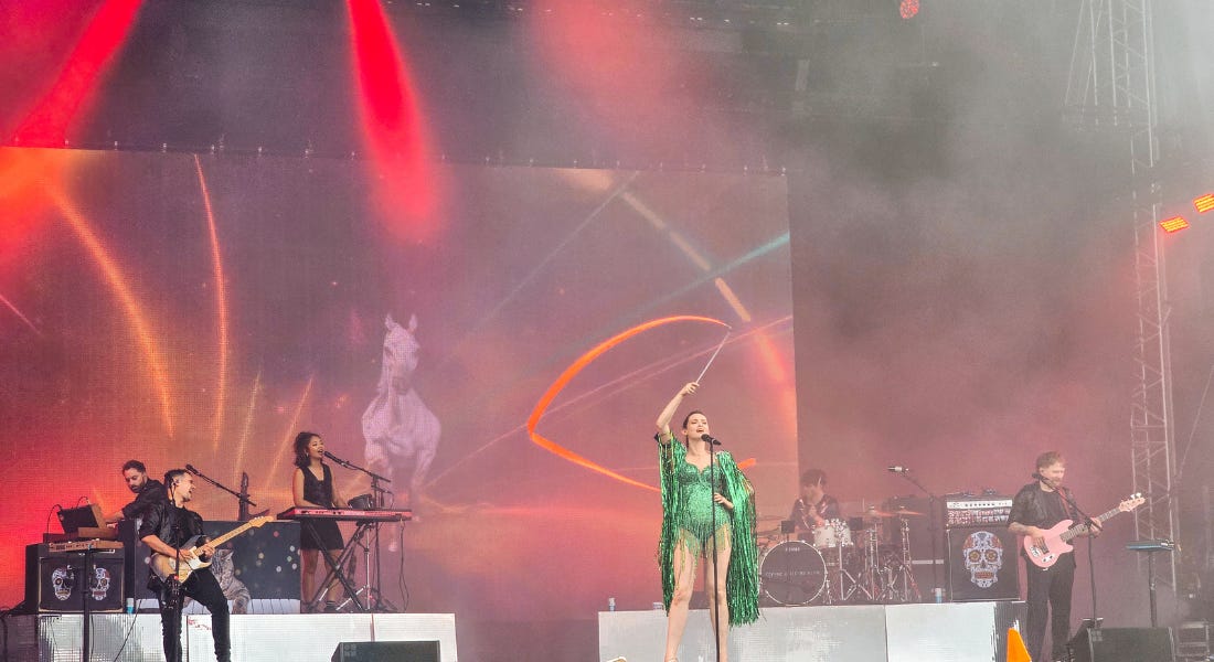 Sophie Ellis-Bextor wearing a sparkly green bodysuit on stage with a band behind her