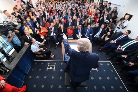 people rising hands as the president points from a lectern