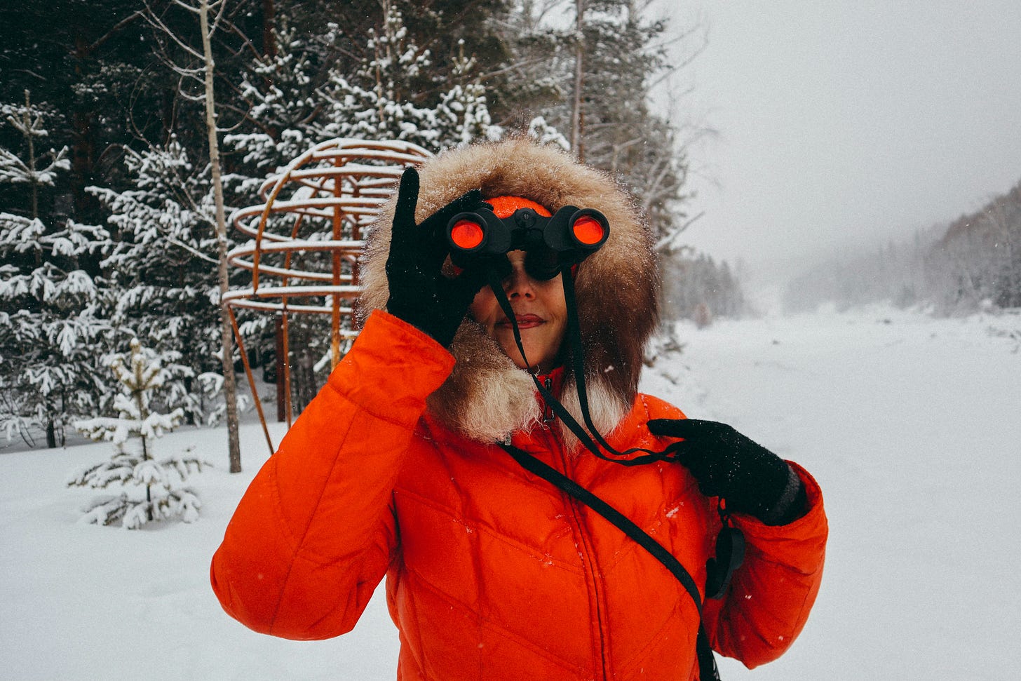 A woman searches a snowy scene with her binoculars