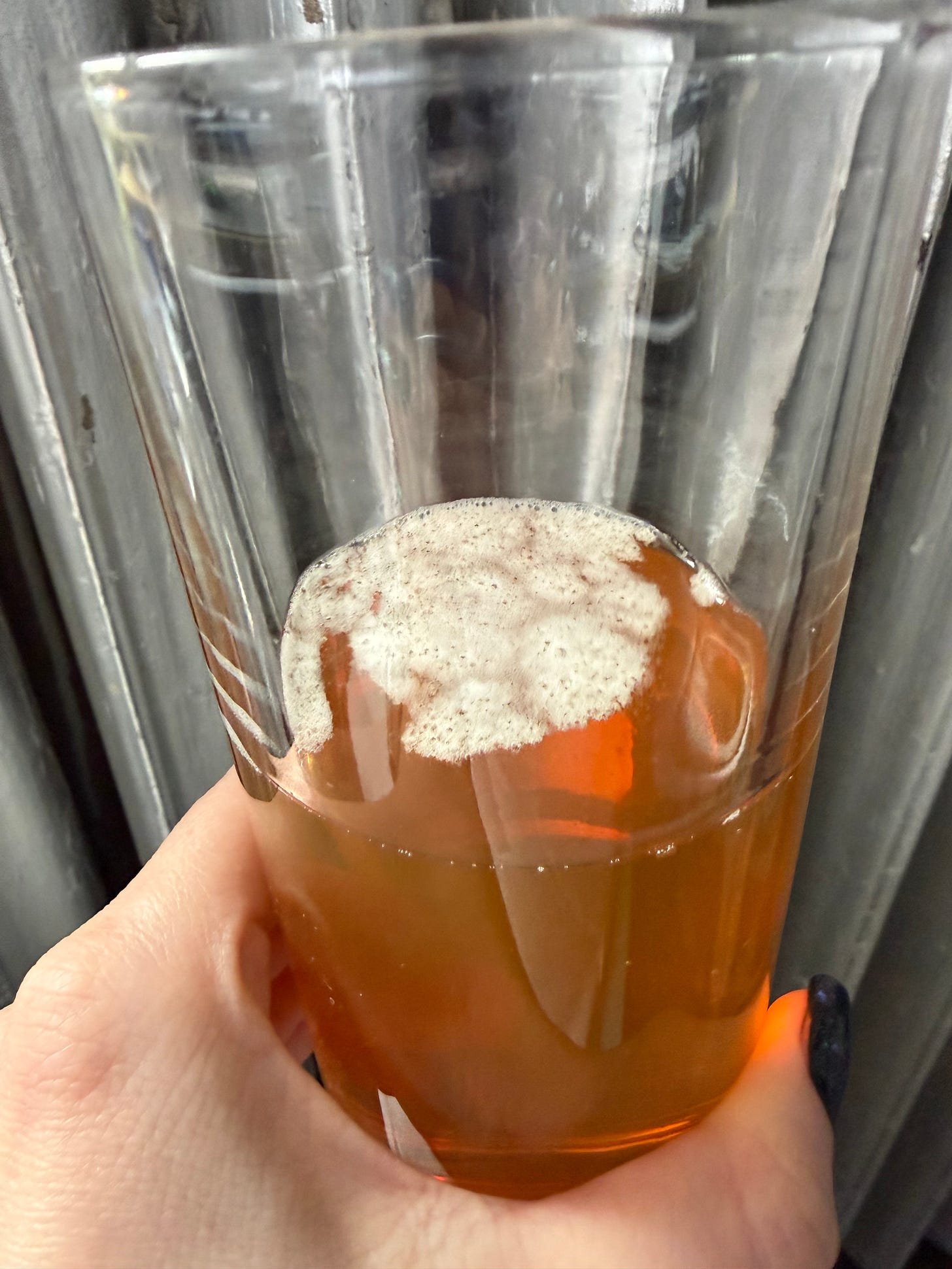 An orange-y brown liquid with a few splotches of white froth on top in a glass An orange-y brown liquid with a few splotches of white froth on top in a glass