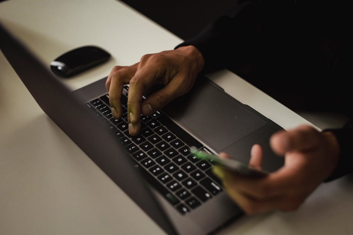 Free Crop faceless man typing on laptop and using smartphone Stock Photo