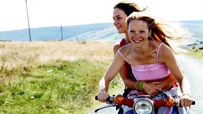 two girls ride a bike through the countryside with the wind blowing in their hair